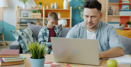 father on laptop and son in background