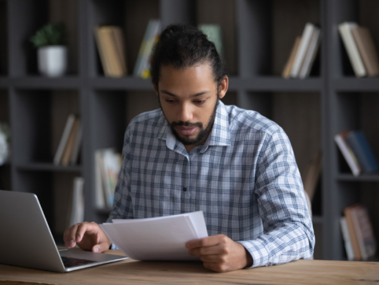 young man looking at document at laptop