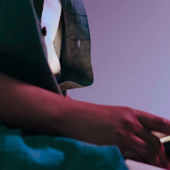 A teenage boy wearing a green garment holds a smartphone in their hands