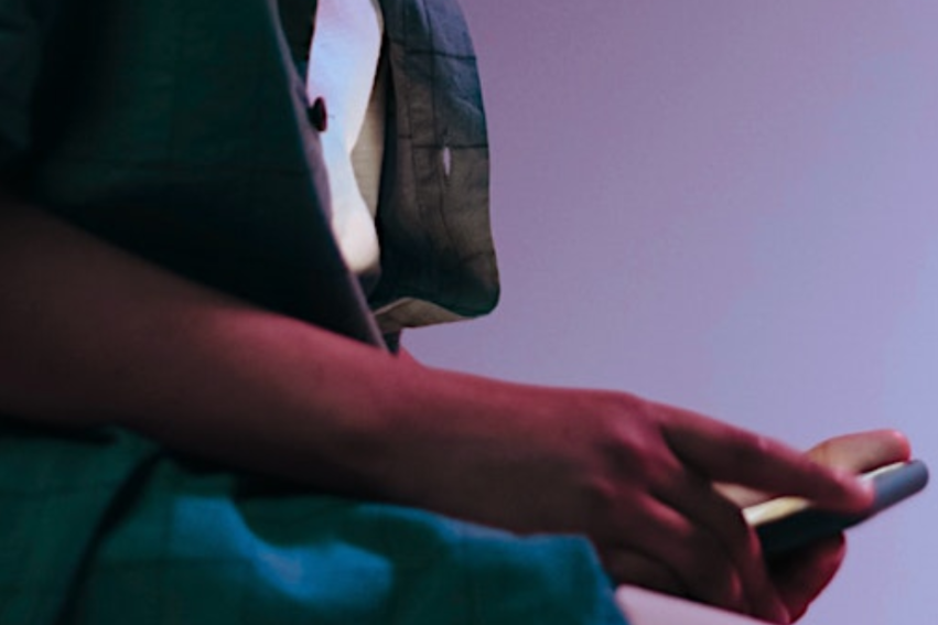A teenage boy wearing a green garment holds a smartphone in their hands