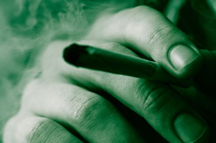 Cannabis weed, a joint in his hands A man smokes . Smoke on a black background. Concepts of medical marijuana use and legalization of the cannabis. On a black background Green Tinting stock photo